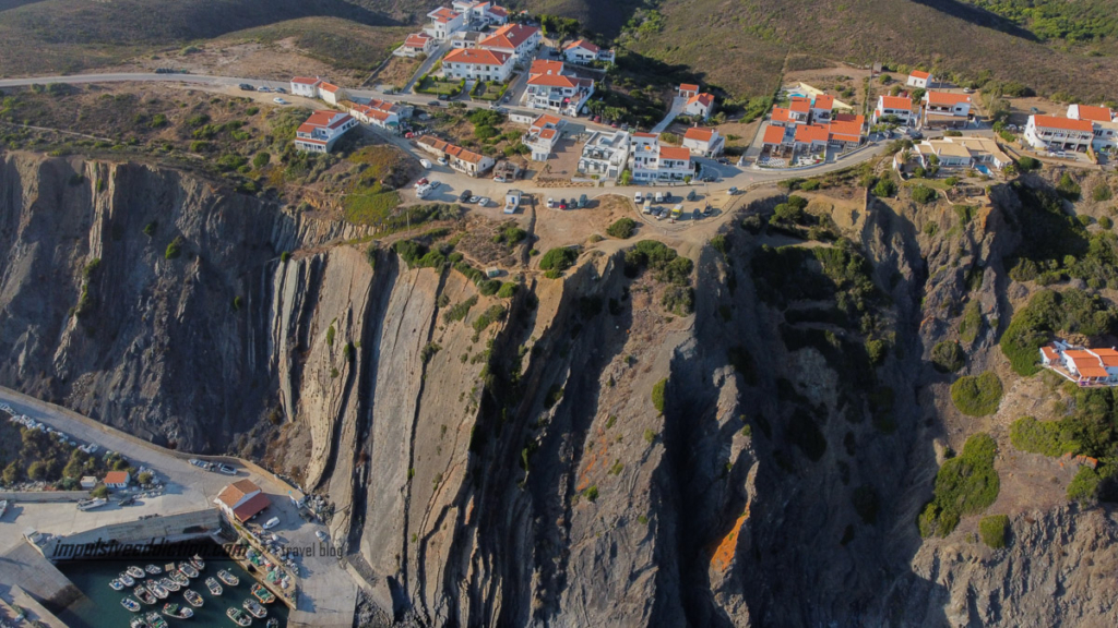 Imagem mais aproximada das falésias escarpadas da Arrifana junto à praia, com as casas no topo e o porto da Arrifana na base da arriba.