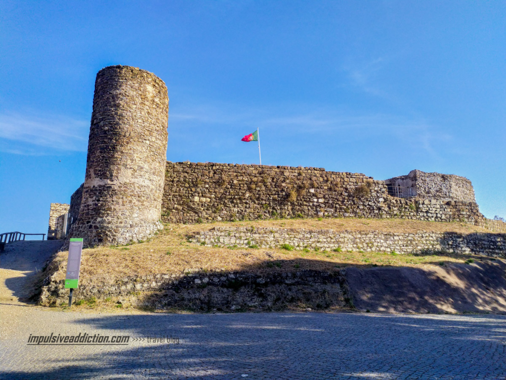 Muralhas do Castelo de Aljezur, com bandeira de Portugal hasteada ao centro.